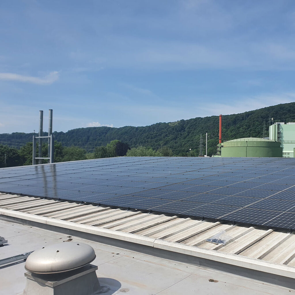 Eine große schwarze Solaranlage auf einem weißen Dach mit grünen Hügeln im Hintergrund