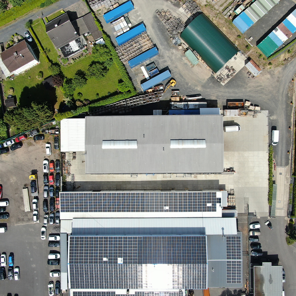 Luftaufnahme eines Industriegebiets mit Hallen, Solarpanelen und geparkten Fahrzeugen