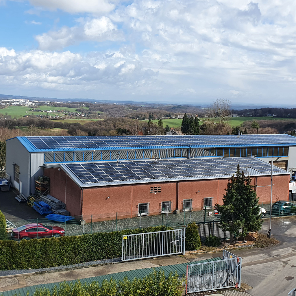 Ein Industriegebäude mit vielen Solarpanels auf dem Dach steht in grüner Landschaft
