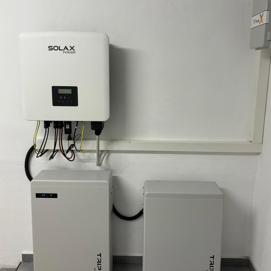 Ein weißer Solax Power Wechselrichter mit Batteriespeichern und sichtbaren Kabeln an der Wand