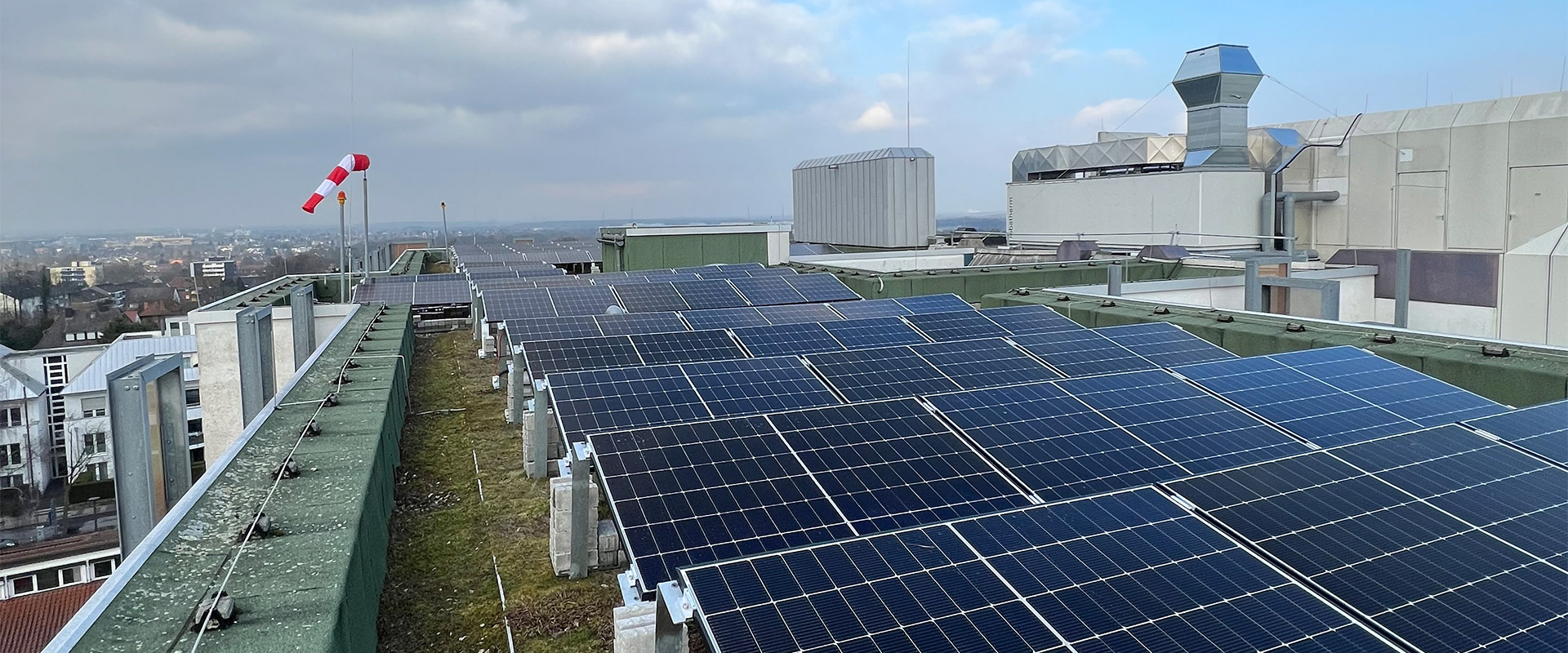 Solarmodule auf einem begrünten Dach unter bewölktem Himmel mit Windsack im Hintergrund