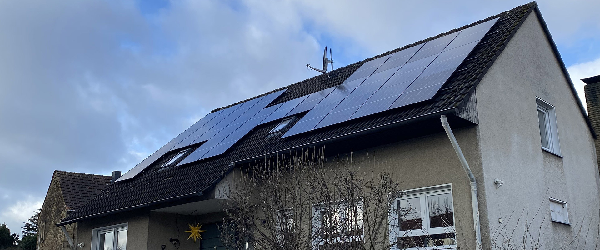 Ein Haus mit schrägem Dach und großen dunklen Solarpaneelen unter wolkigem Himmel