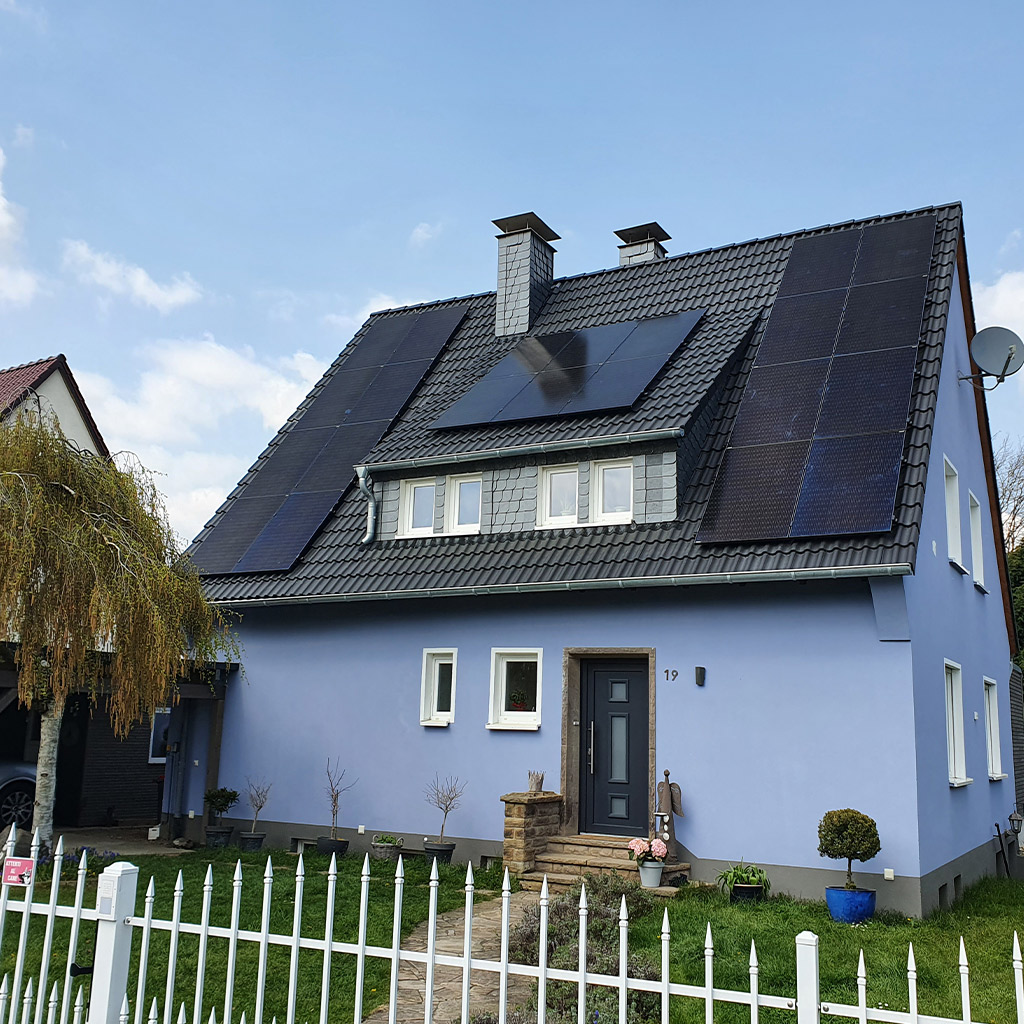 Blaues Einfamilienhaus mit grauem Dach und vielen Solarpaneelen im Garten