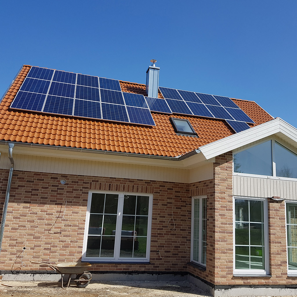 Ein Einfamilienhaus mit roten Ziegeln und Solarpanelen auf dem Dach vor blauem Himmel