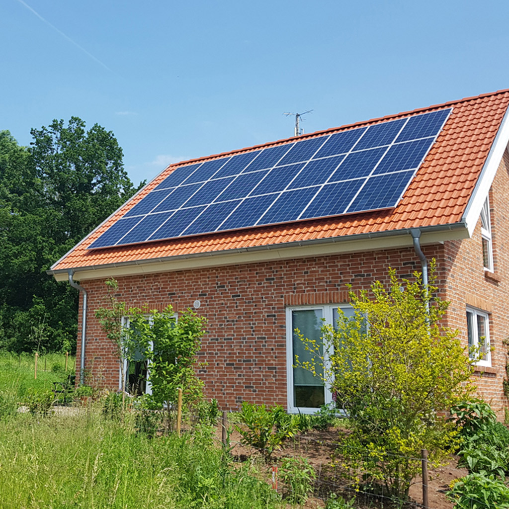 Rotes Backsteinhaus mit Solarpanels auf dem Dach und umgeben von viel Grün