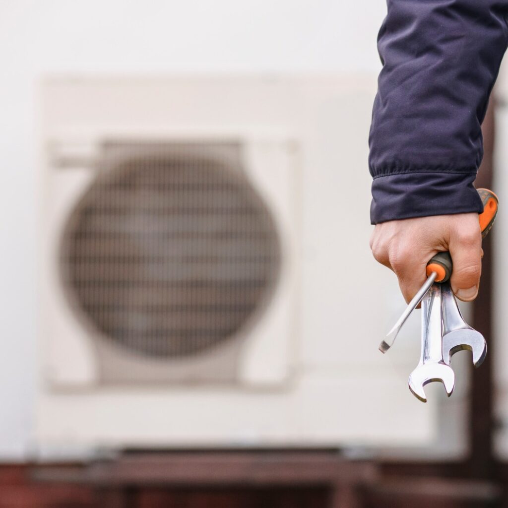 Installation und Wartung von Wärmepumpen-Heizsystemen. Arbeiterhand mit Werkzeugen vor dem Hintergrund einer Wärmepumpe. Heizen und Kühlen mit Wärmepumpen.