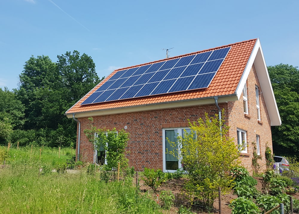 Ein rotes Ziegelhaus mit Solarpanelen auf dem Dach steht im grünen Garten