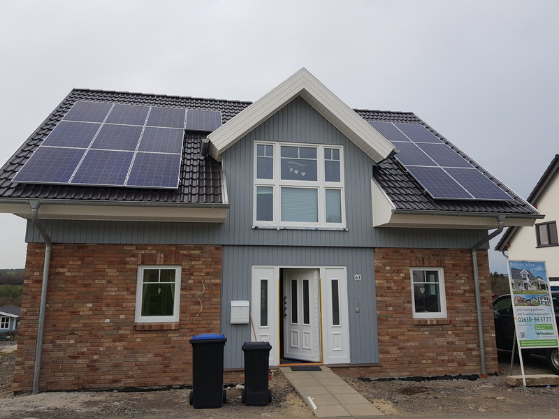 Modernes Einfamilienhaus mit Solarpaneelen auf dem Dach und zwei Mülltonnen davor