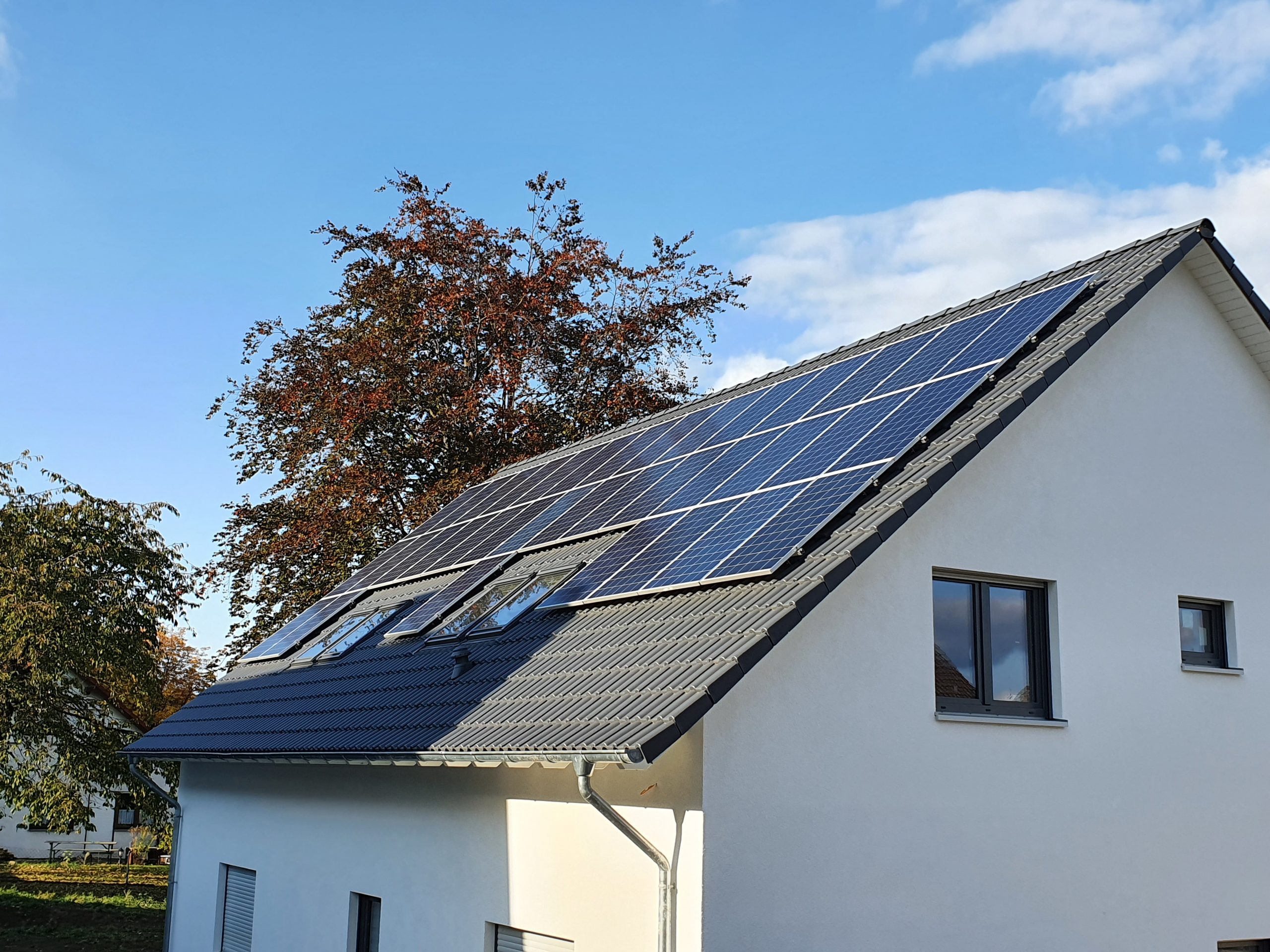 Modern weißes Einfamilienhaus mit dunklem Dach und großen Solarpaneelen unter blauem Himmel
