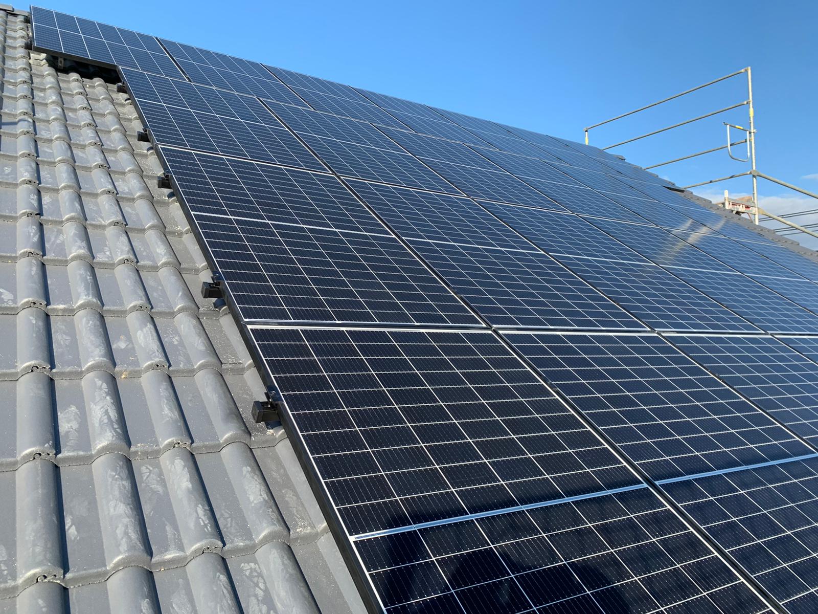 Große schwarze Solarpaneele auf einem grauen Ziegeldach unter blauem Himmel