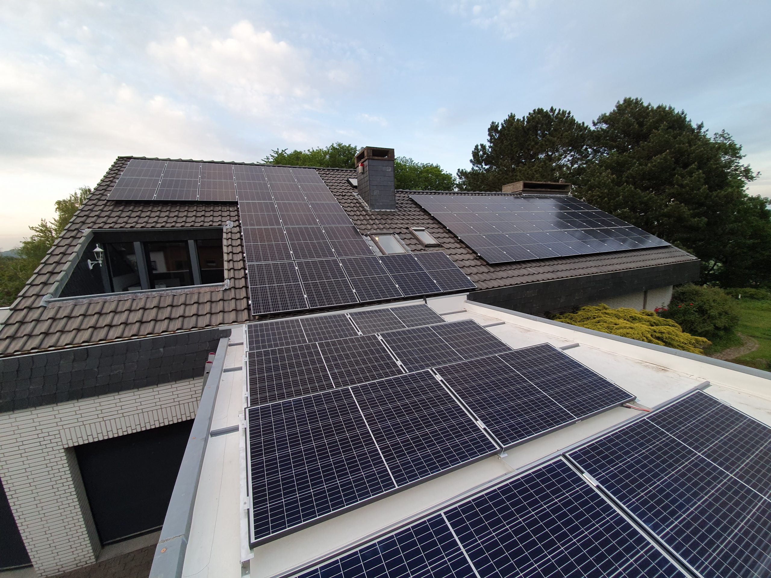 Ein modernes Haus mit vielen blauen Solarpanels auf mehreren Dächern und grünen Bäumen