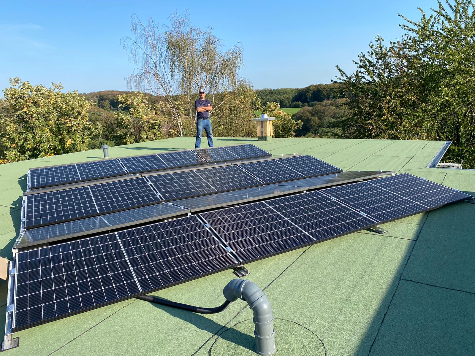 Ein Mann steht nachdenklich auf einem grünen Flachdach mit schwarzen Solarpanels