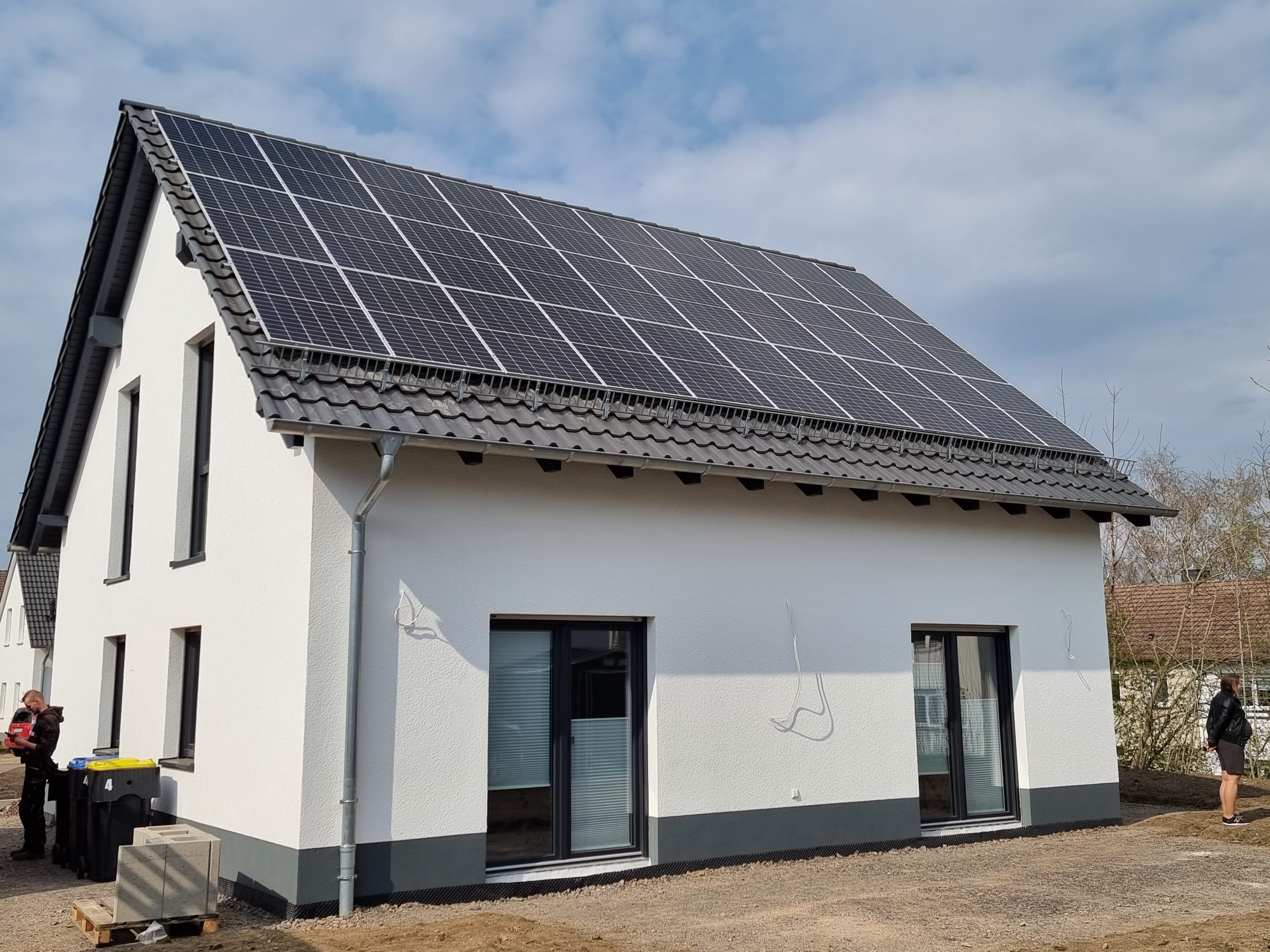 Weißes Einfamilienhaus mit grauem Dach und großen Solarpaneelen auf dem Dach