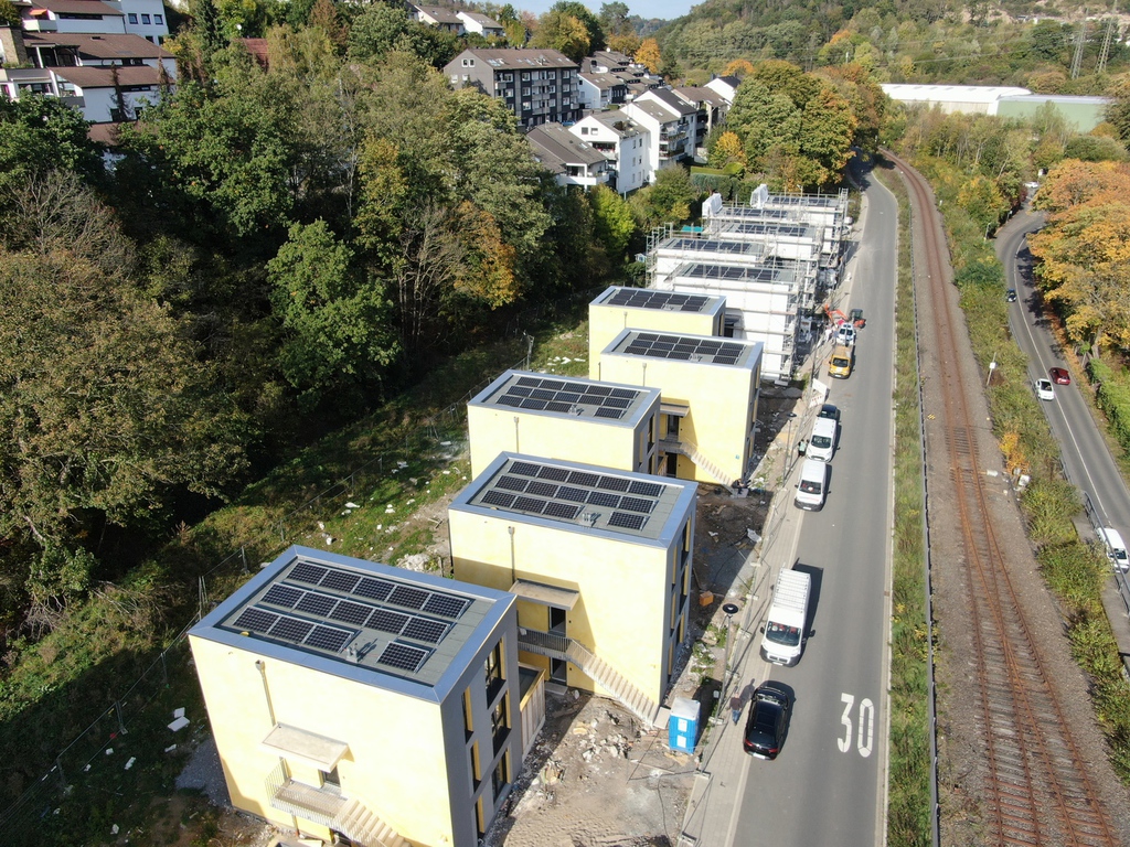 Gelbe Neubauten mit Solaranlagen am Dach stehen neben einer Straße und Bahngleisen