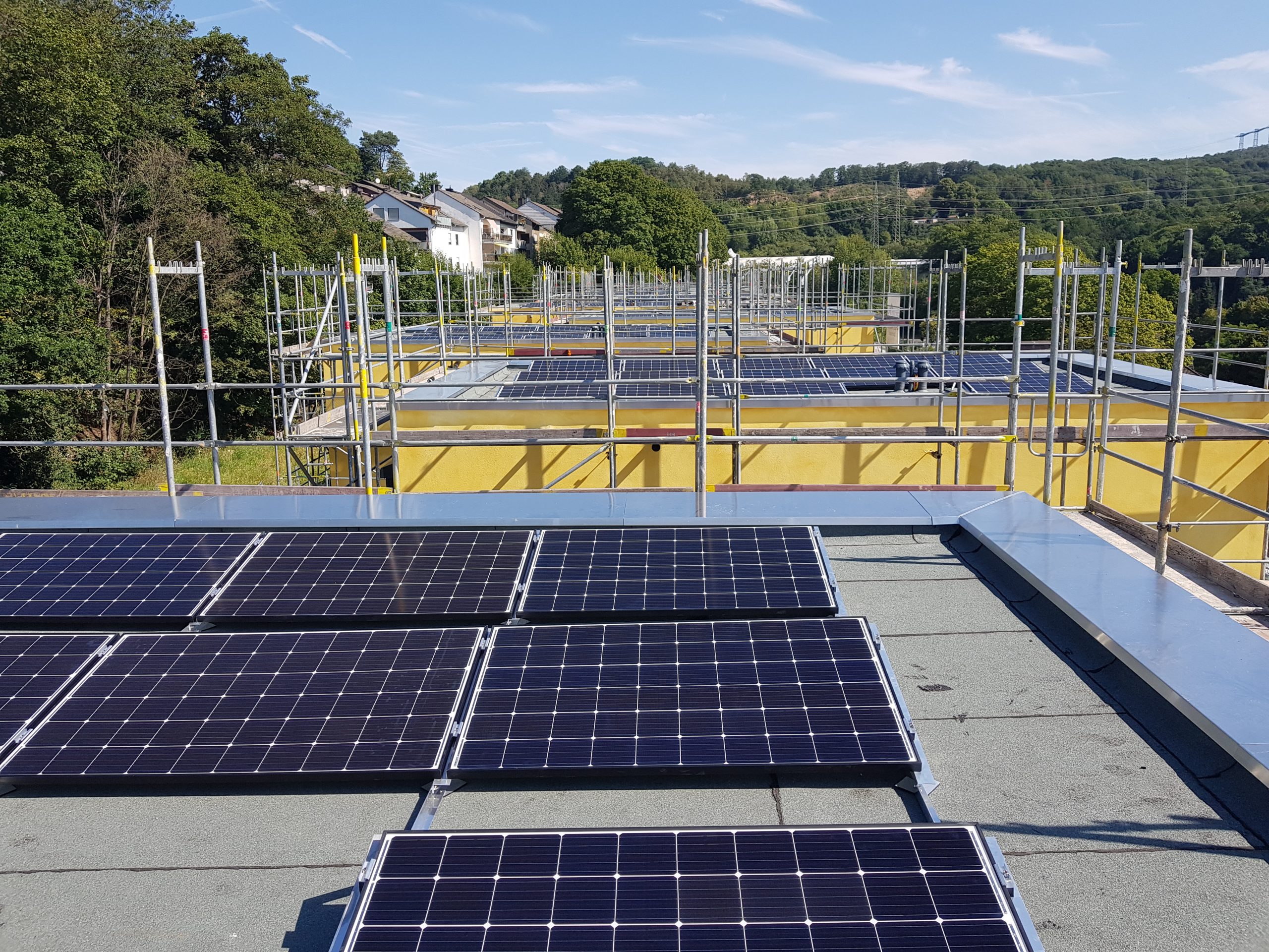 Solarmodule auf einem Flachdach mit gelbem Gebäude und Baugerüsten im Hintergrund