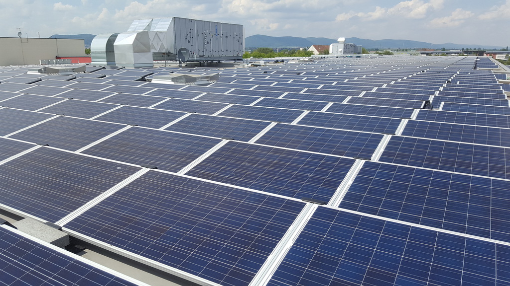 Viele blaue Solarpanels auf einem großen Flachdach unter leicht bewölktem Himmel