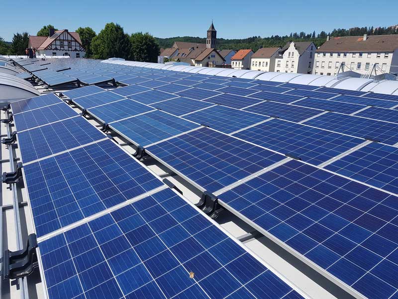 Eine große Fläche mit blauen Solarpaneelen auf einem Dach in einem Dorf im Sommer