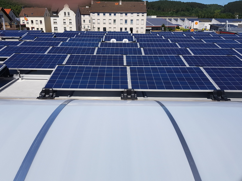 Viele blaue Solarpanels auf einem Dach vor weißen Wohnhäusern im Sonnenlicht