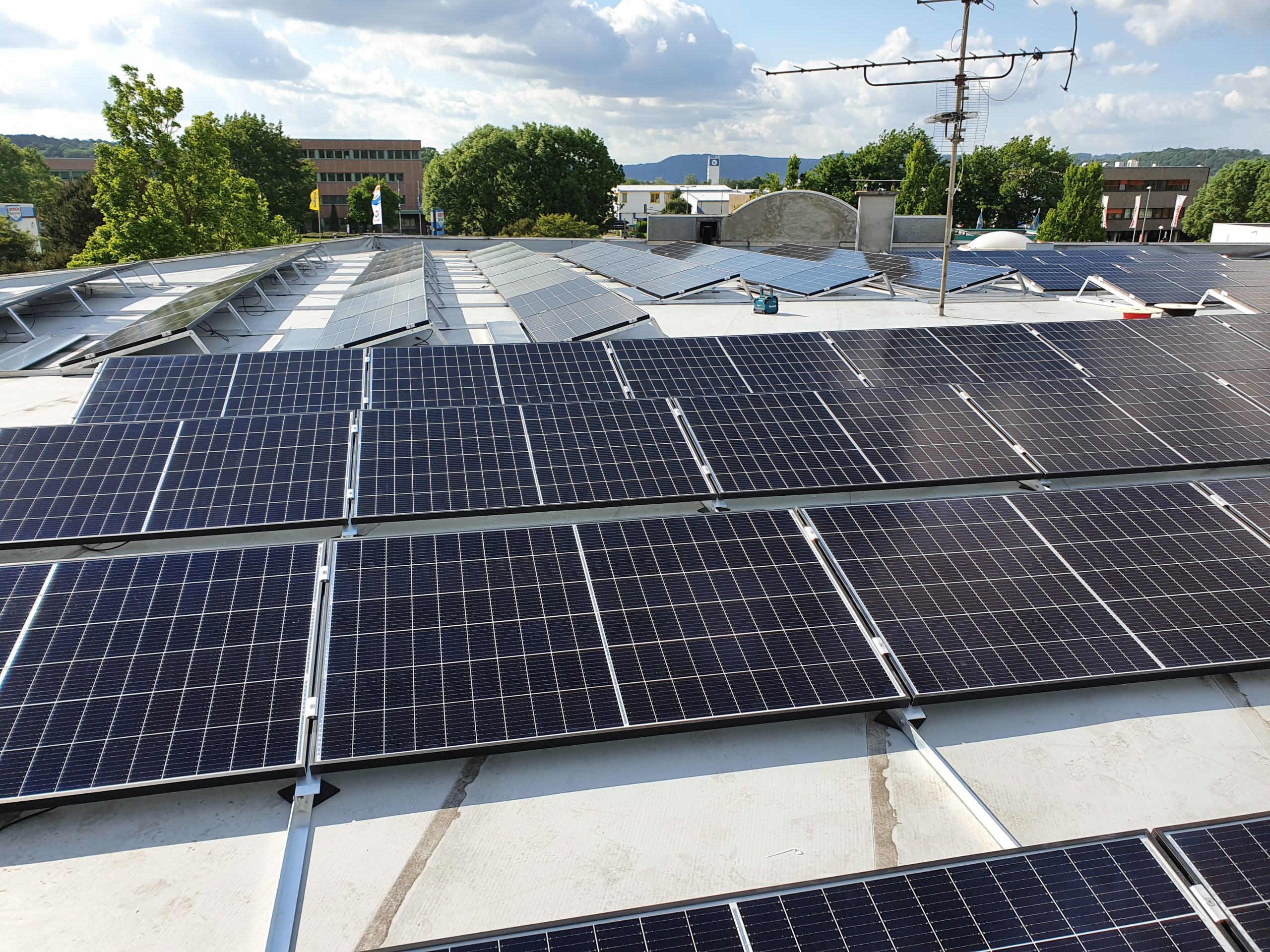 Viele dunkle Solarpanels auf einem Flachdach unter blauem Himmel mit weißen Wolken