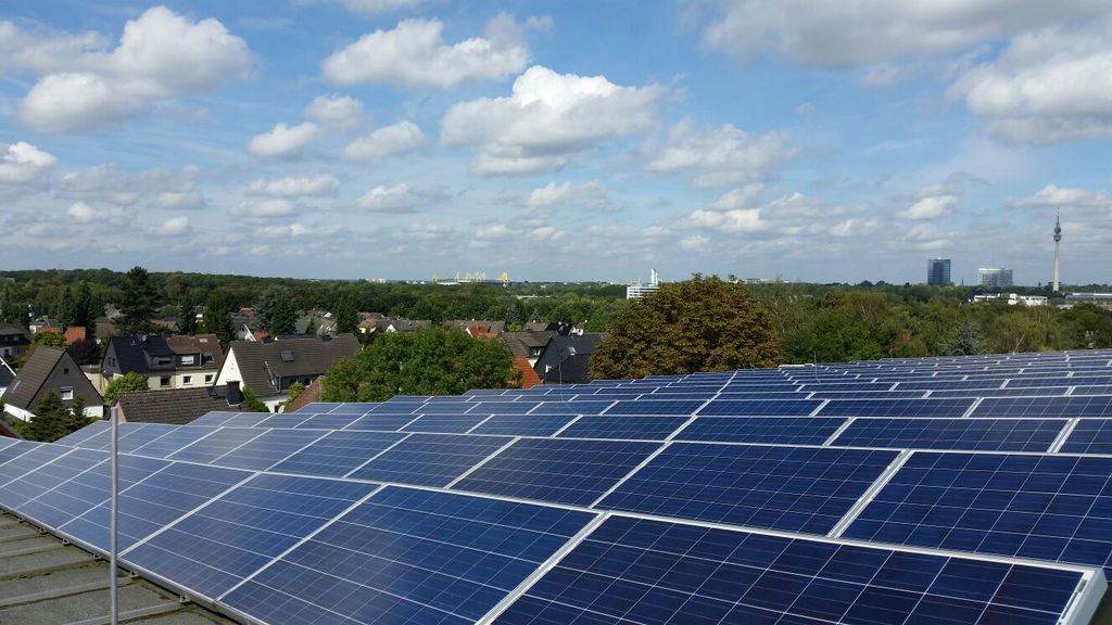 Solarmodule glänzen auf einem Dach vor einem weiten Blick über eine grüne Stadtlandschaft