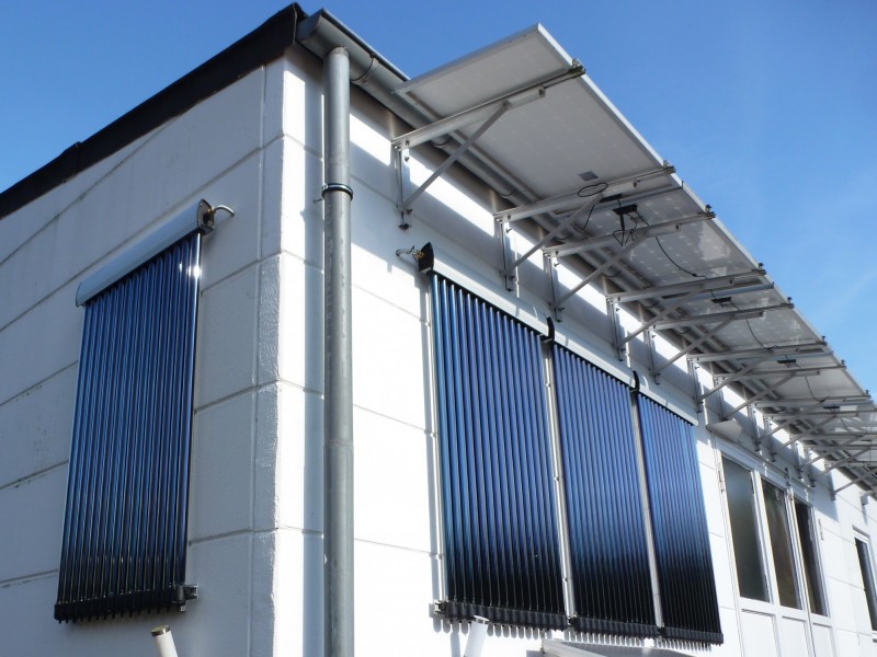 Ein weißes Gebäude mit Solarpaneelen und Röhrenkollektoren an der Fassade