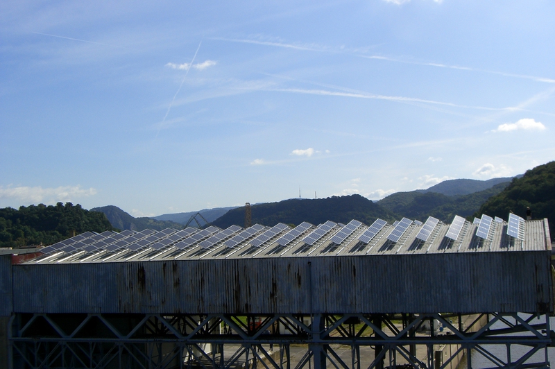 Ein großes Hallendach mit Photovoltaikanlage vor bewaldeten Hügeln im Sonnenlicht