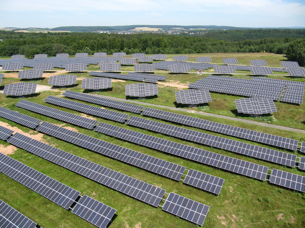 Ein großes Solarfeld mit vielen schwarzen Solarmodulen auf grünem Gras unter blauem Himmel