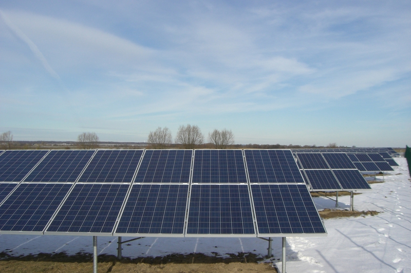 Eine große Solaranlage mit blauen Panels steht auf schneebedecktem Boden unter blauem Himmel