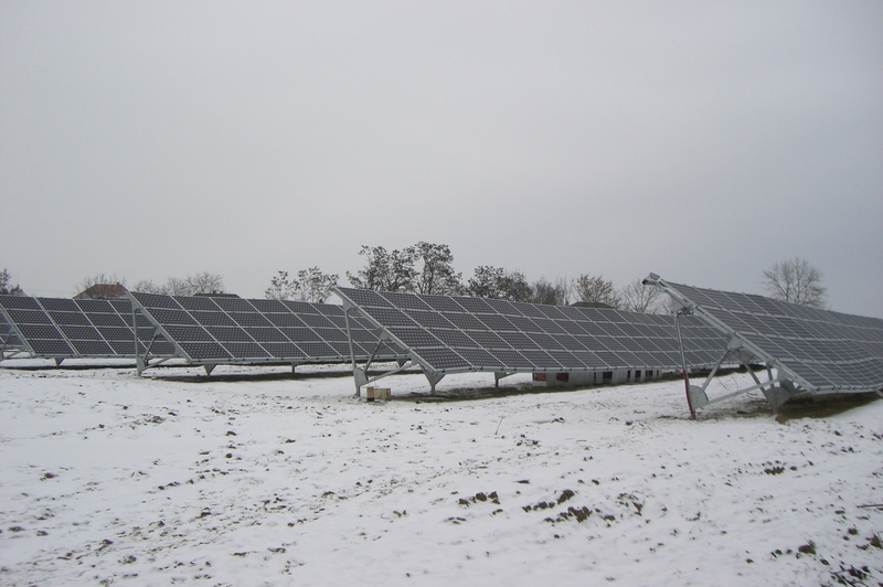 Mehrere dunkle Solarpanels stehen schräg auf einer schneebedeckten Wiese im Freien