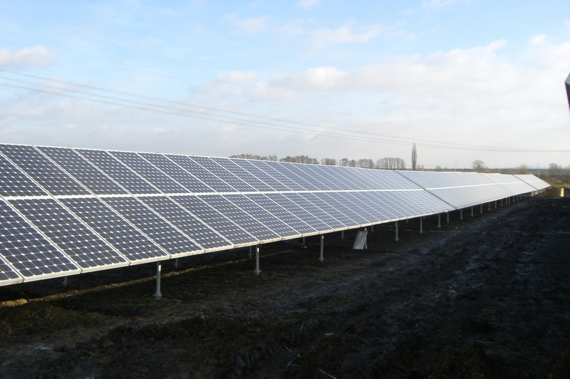 Eine Reihe von blauen Solarpaneelen steht auf einem Feld unter bewölktem Himmel