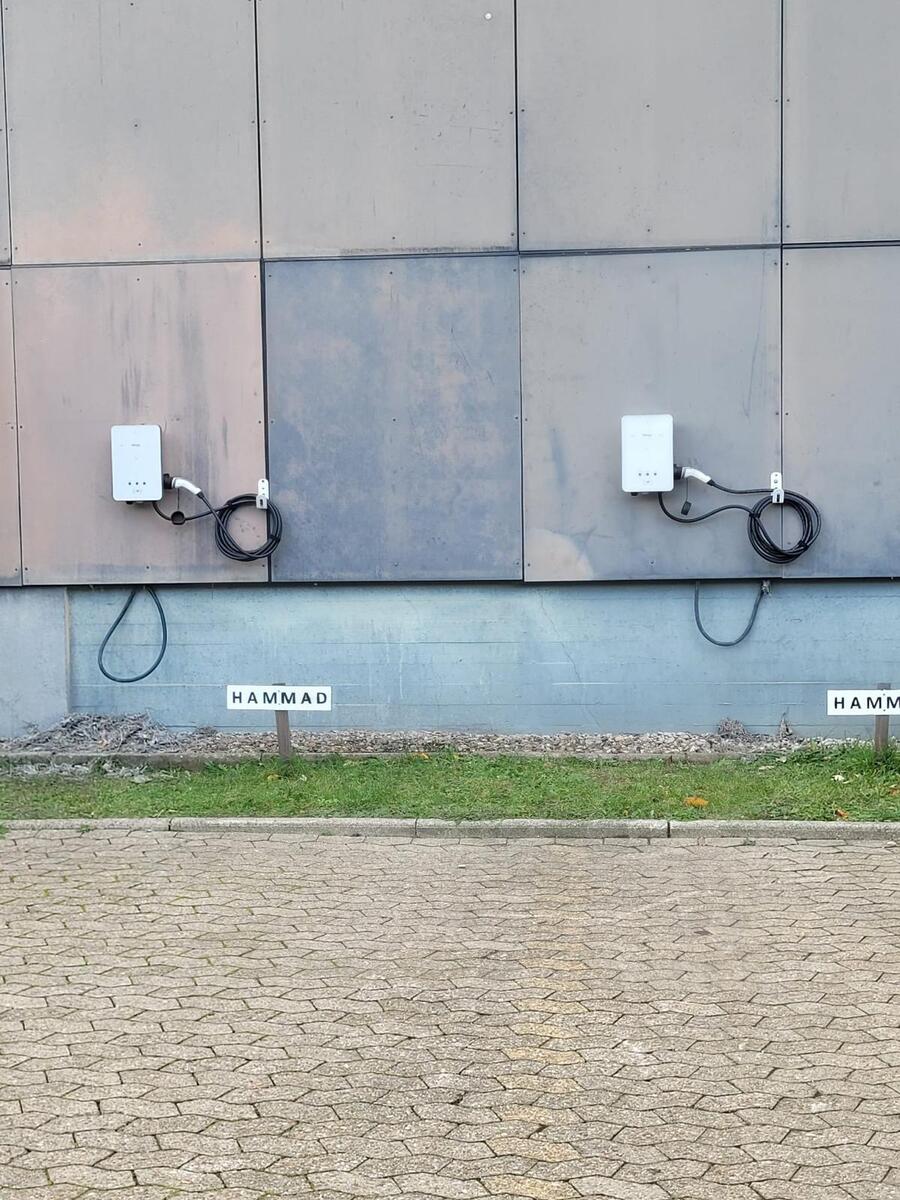 Zwei weisse Wandgeraete mit schwarzen Kabelschlaufen an grauer Fassade