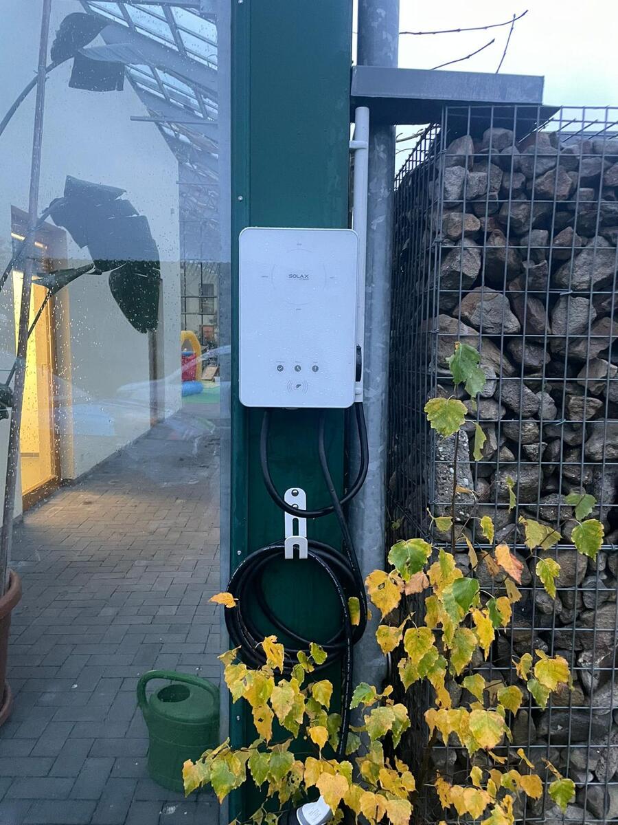 Weisses Wandgeraet mit Kabeln am Pfosten neben Steinwand und Weinlaub