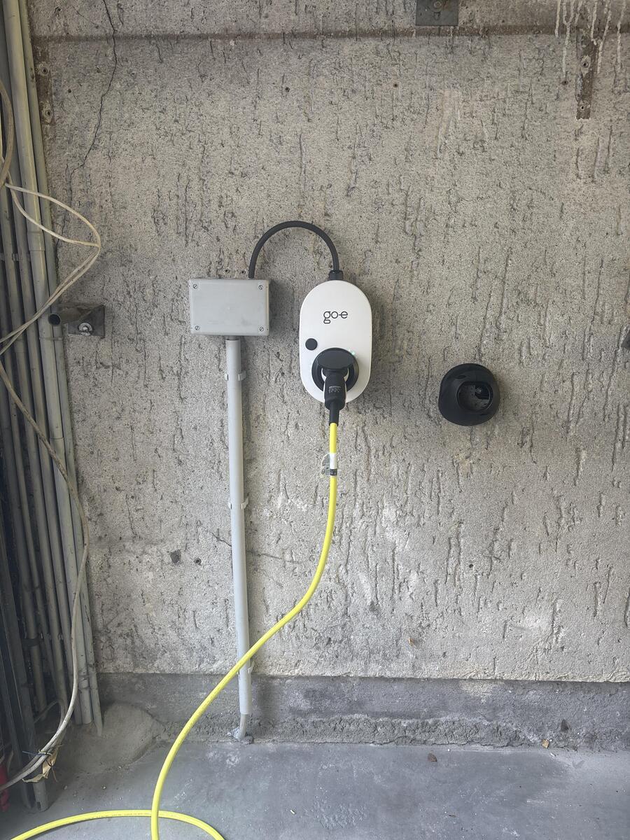 Weisse Wallbox mit Kabel und gelbem Ladekabel an grauer Betonwand