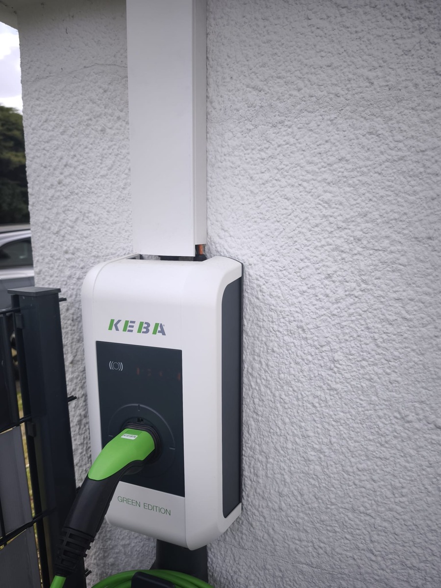 Weiße KEBA Wallbox mit grünem Ladestecker an rauer Hauswand