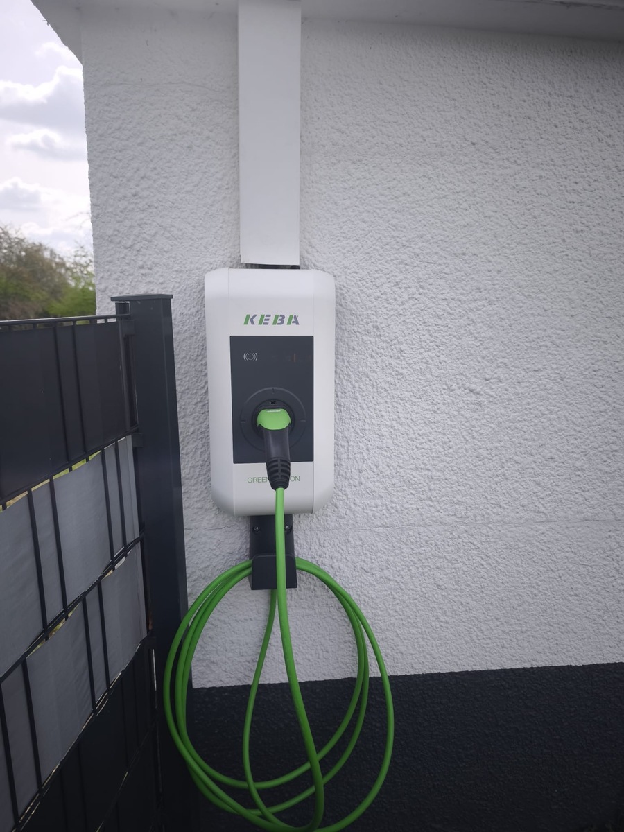 Weiße KEBA Ladestation mit grünem Kabel an grauer Wand, neutraler Look