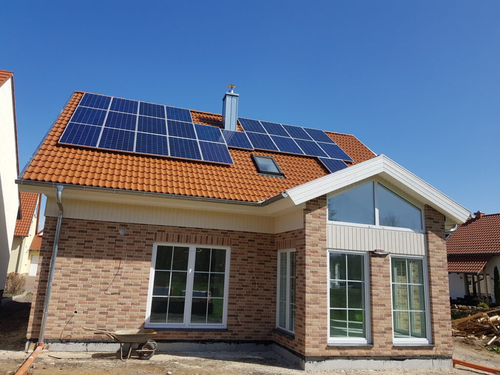Backsteinhaus mit Solarmodulen auf rotem Ziegeldach vor blauem Himmel