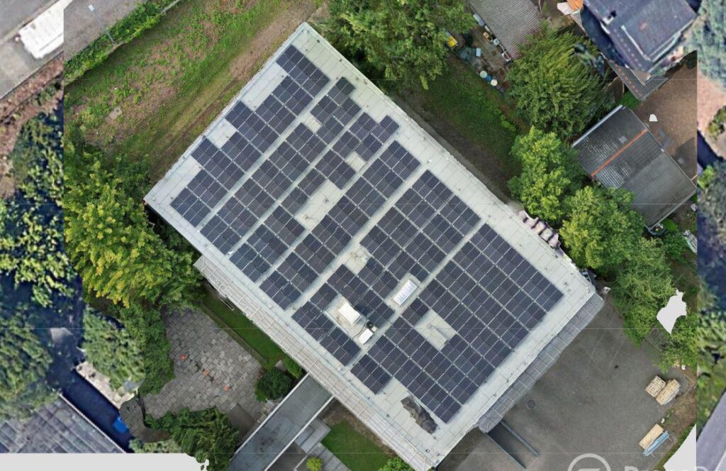 Luftaufnahme eines Gebaeudedachs mit vielen blauen Solarmodulen umgeben von Baeumen