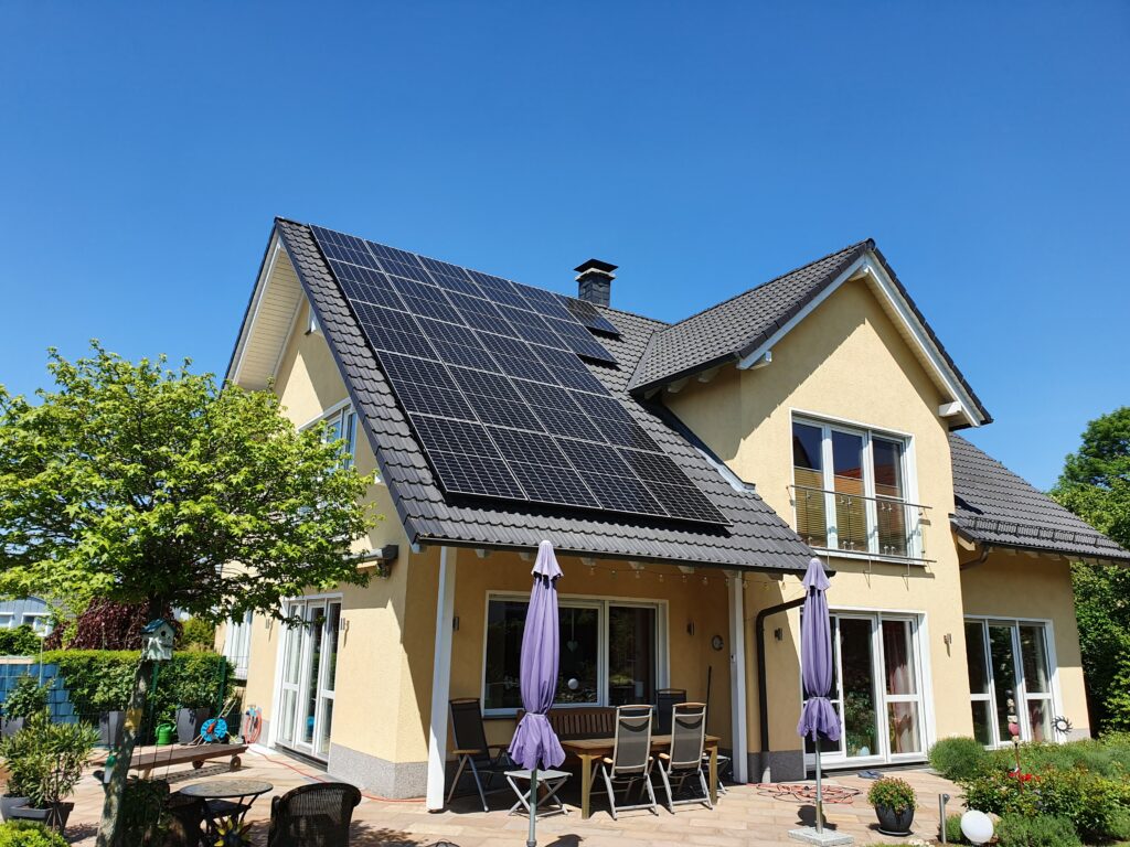 Gelbes Einfamilienhaus mit Solaranlage auf dem Dach und Terrasse mit Sonnenschirmen